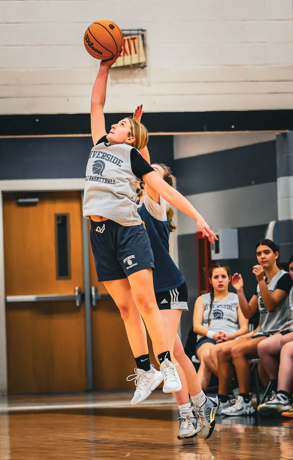 Basketball player leaps high to make a shot during competitive game action.