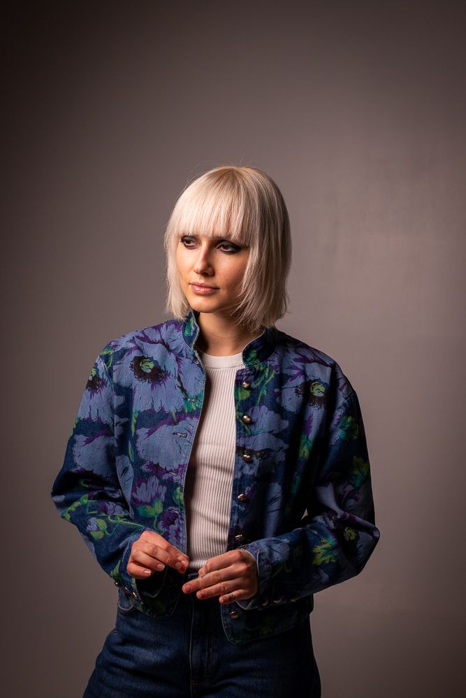 Fashion portrait featuring floral blue bomber jacket and white top against grey backdrop.