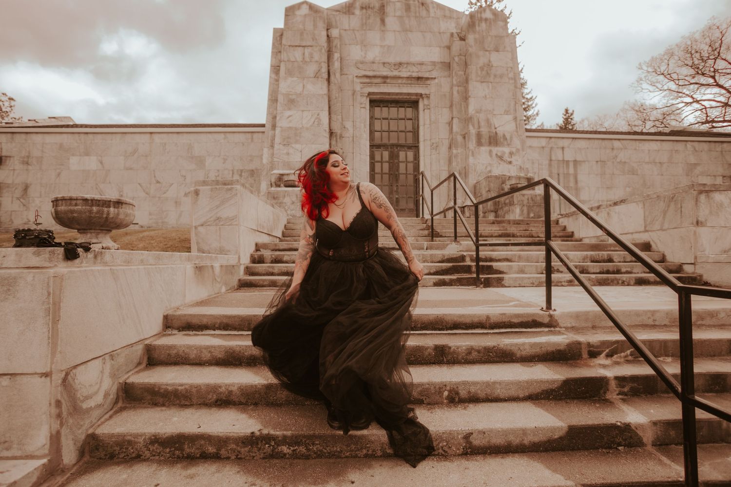 A flowing black dress contrasts against stone steps of a historic building in sepia tones.