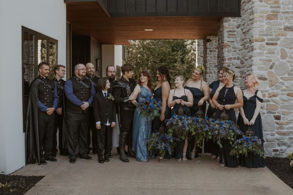 Wedding party in blue and black attire poses together under a covered entrance.