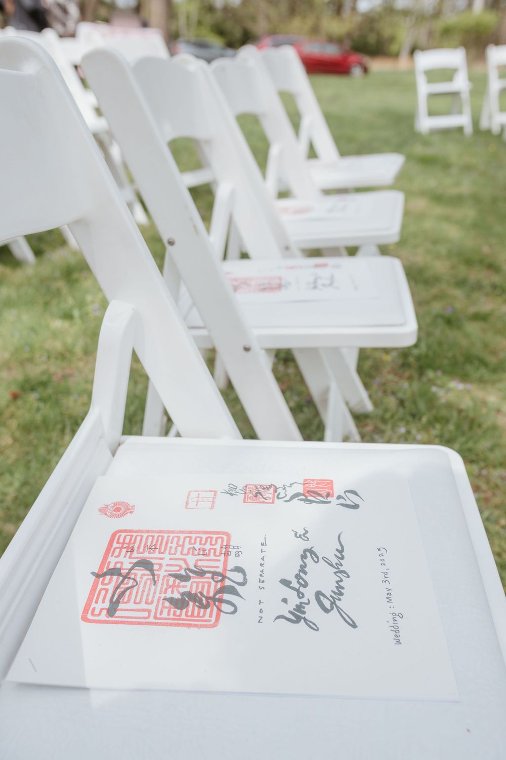 White folding chairs arranged outdoors with a red signature stamp visible on one seat.