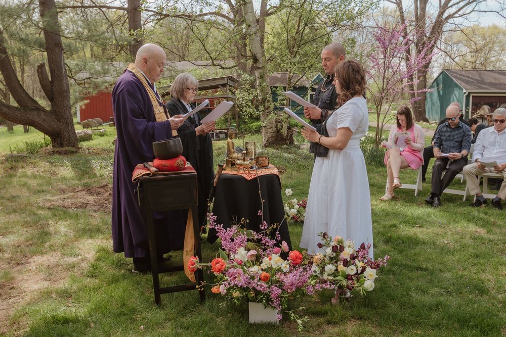 An intimate outdoor spring wedding ceremony surrounded by blooming trees and floral arrangements on the lawn.