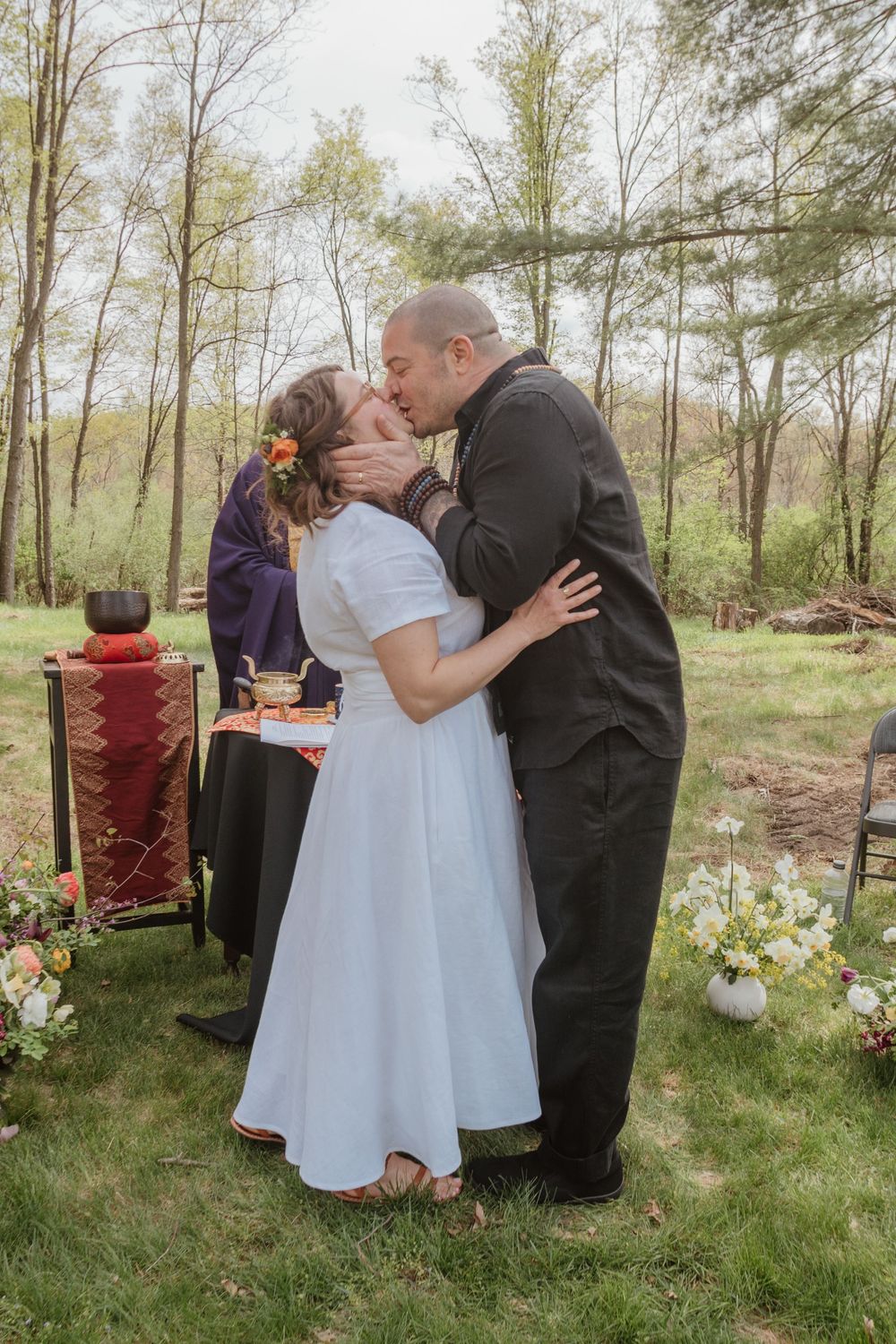 A couple shares their first kiss as newlyweds during an outdoor wedding ceremony with floral decorations.