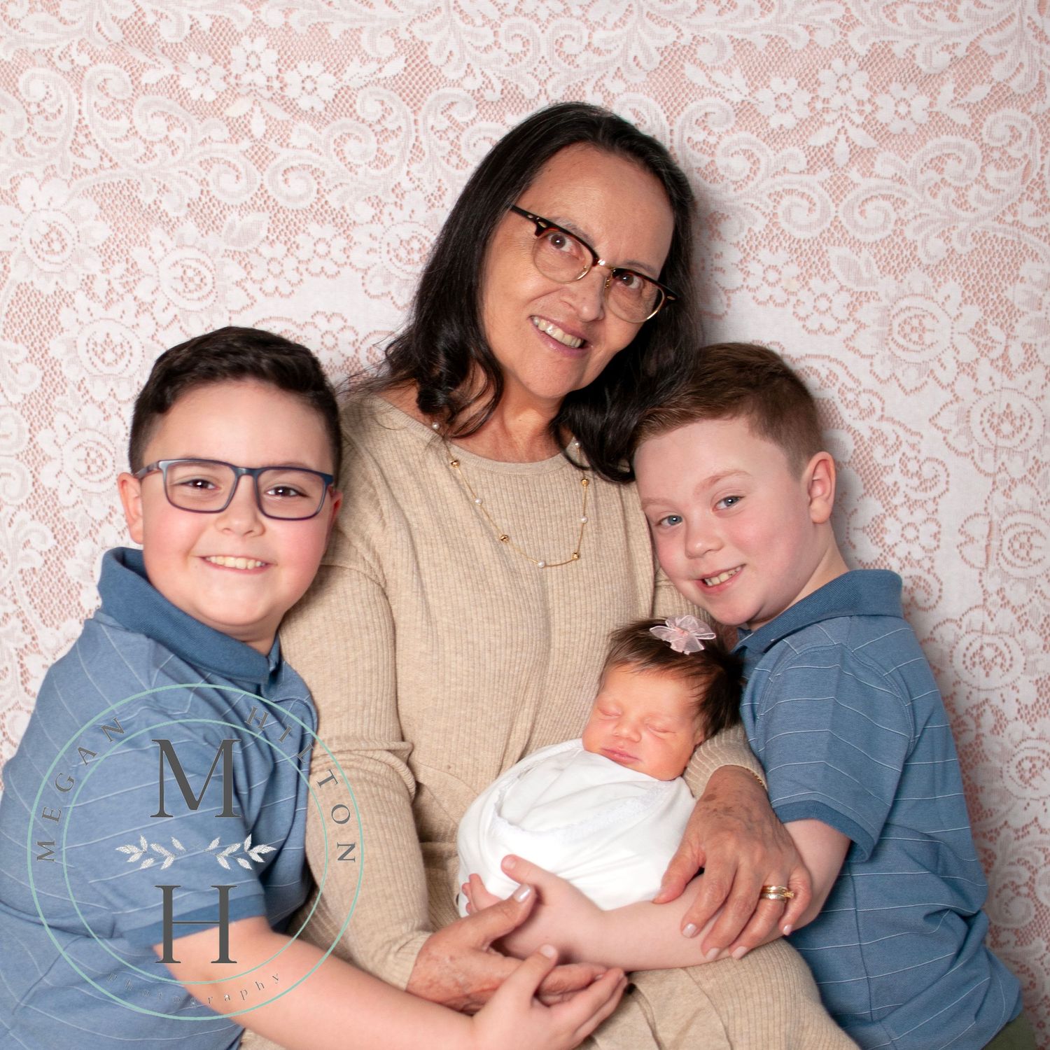 Multigenerational photo of grandmother with three young grandchildren including a newborn on a pink lacy backdrop
