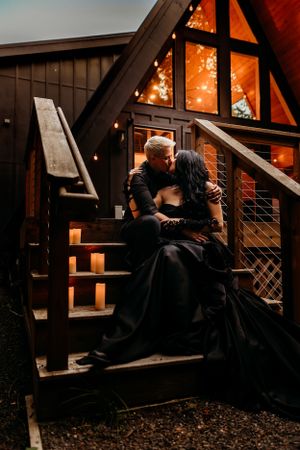 A couple sits romantically on wooden stairs of a cabin decorated with string lights.