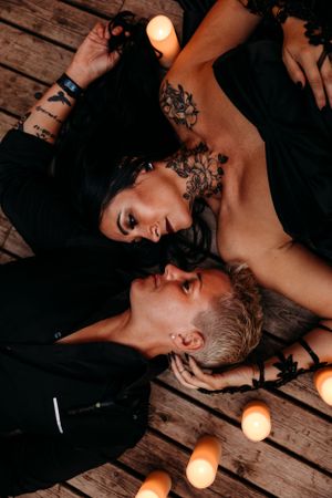 An artistic overhead shot of a couple lying on wooden decking surrounded by candles.