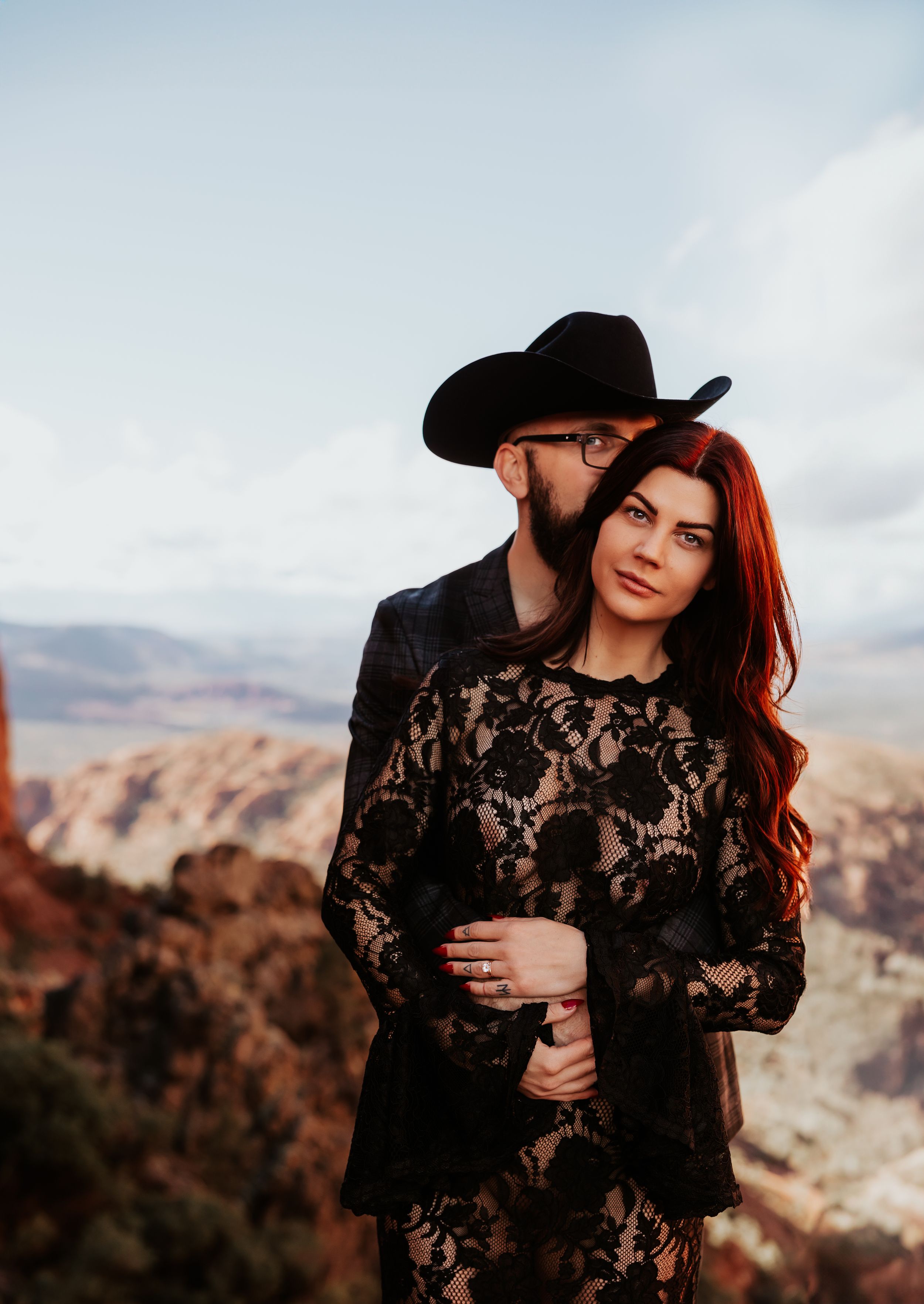 A couple in black formal wear poses against a backdrop of desert canyons.