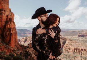 A tender moment between a couple in black attire with red rock canyon views behind them.