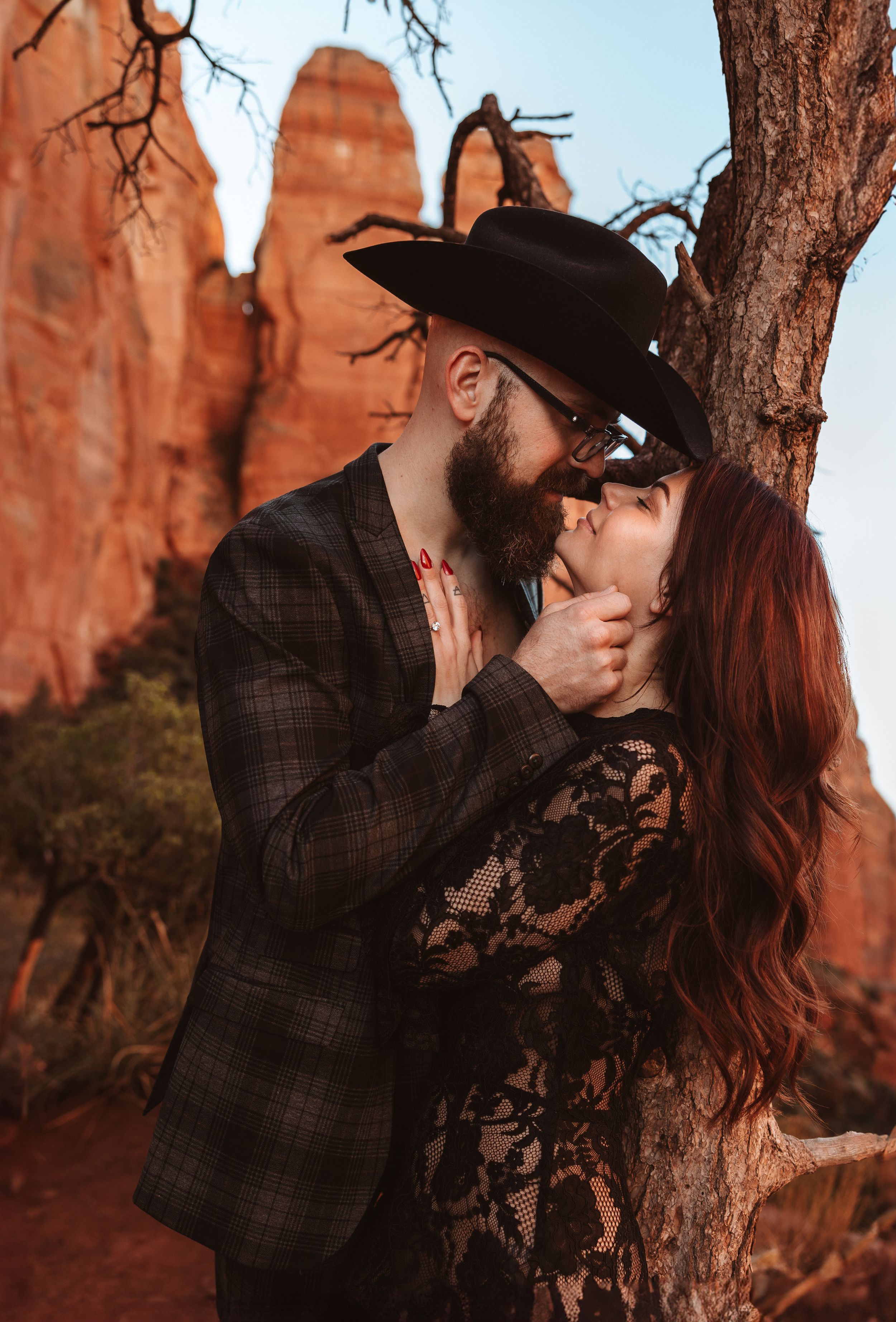 A romantic moment captured between a couple in formal attire against Sedona's red rock cliffs.