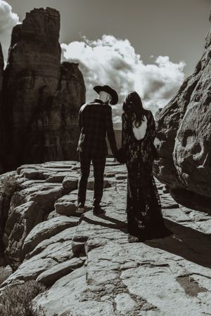 A couple in black attire walks along dramatic rock formations in black and white photography.