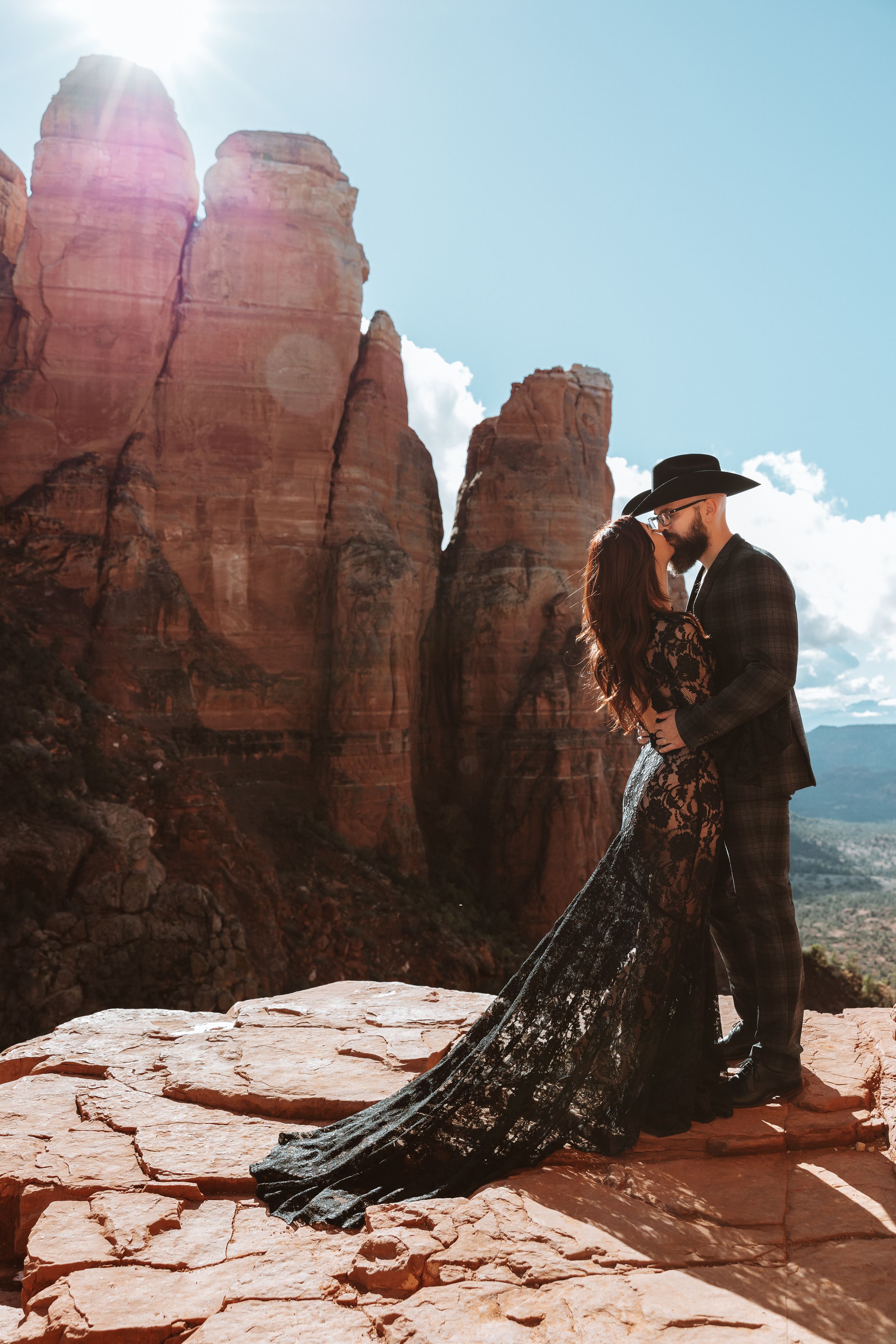 A romantic couple in western attire poses against dramatic red rock formations at a scenic overlook.