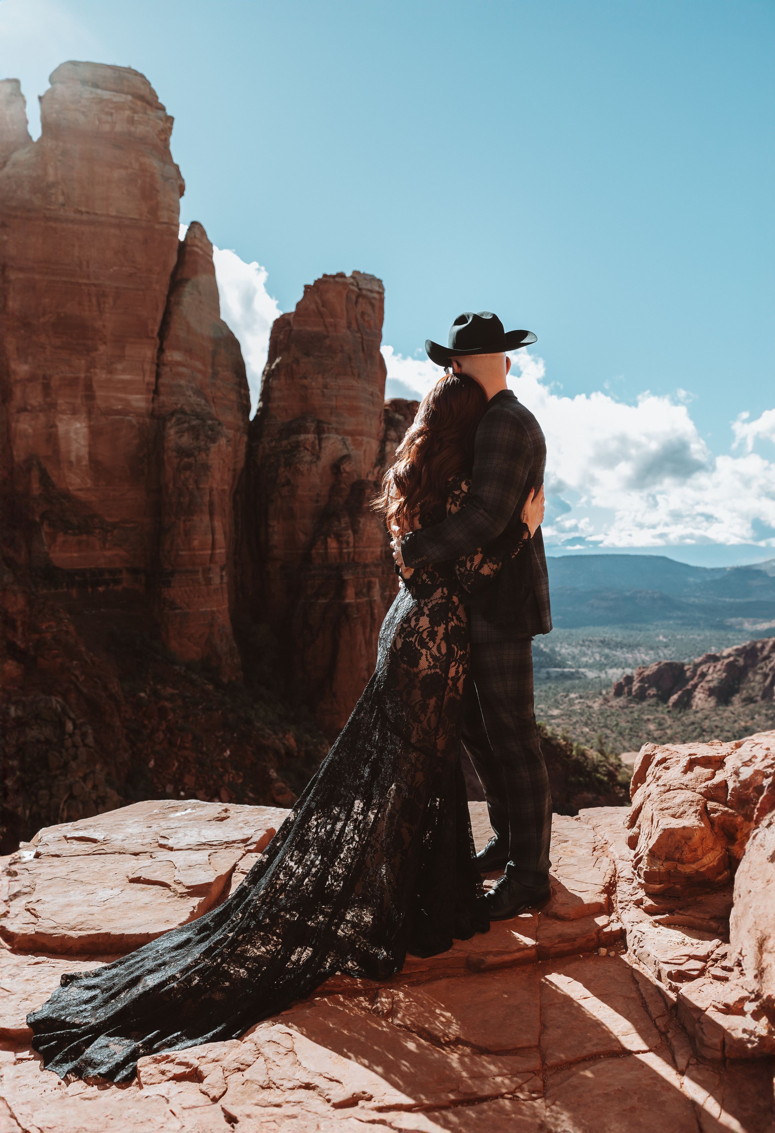 A silhouetted couple in formal wear stands near towering red rock spires at sunset.