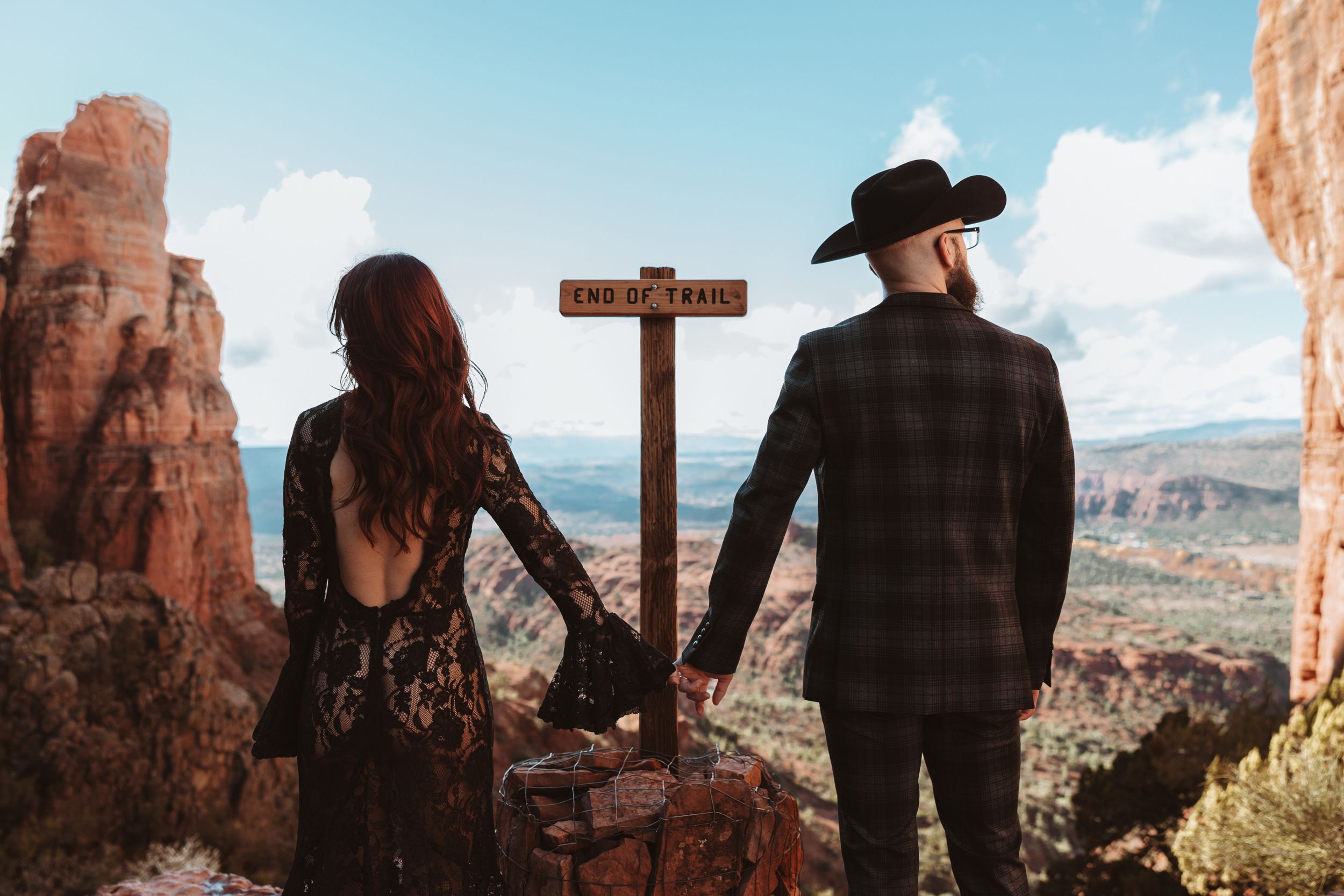 A couple stands near a wooden trail marker surrounded by majestic red rock formations in Sedona, AZ.
