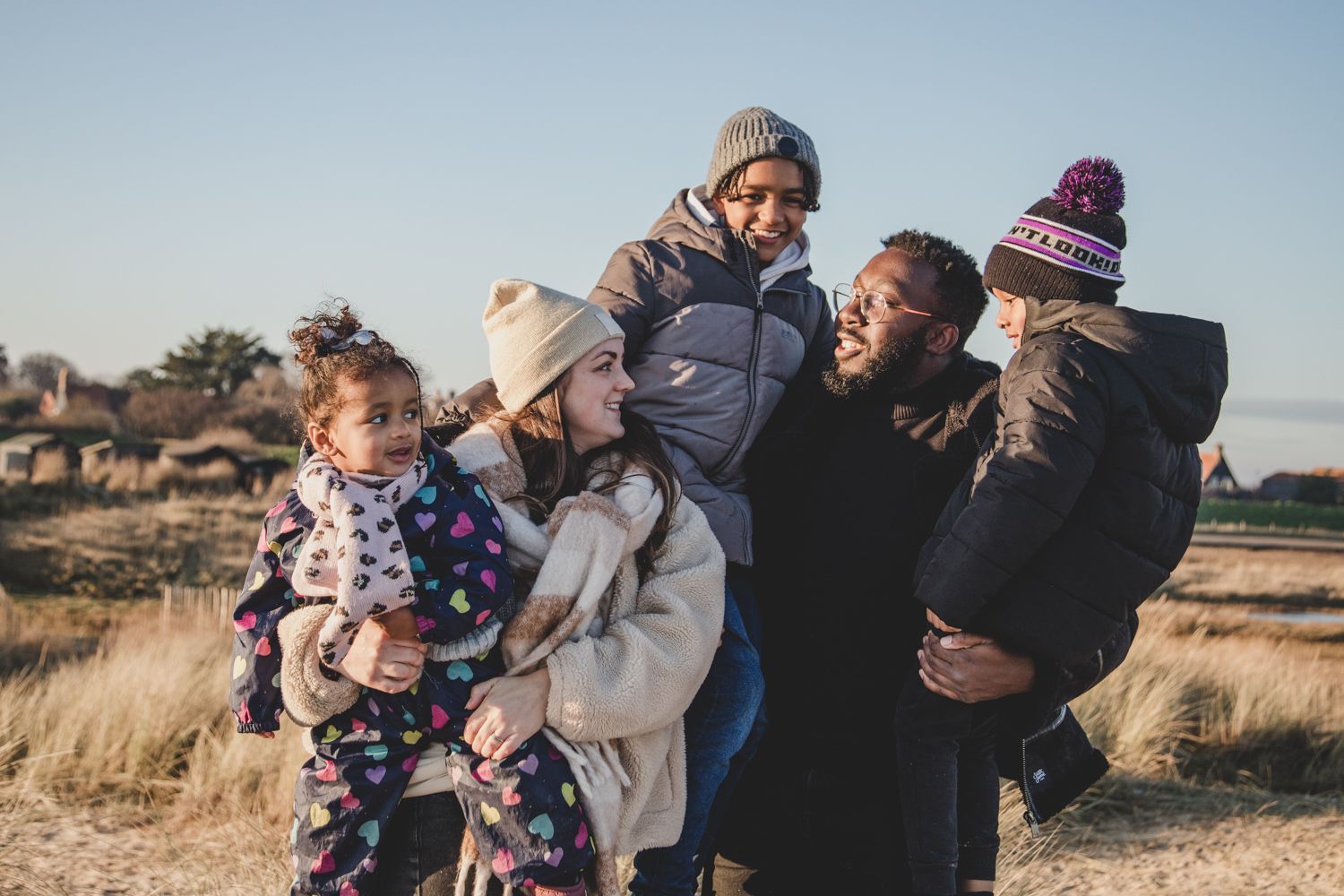 Group bundled in winter clothes sharing embrace on grassy hillside.