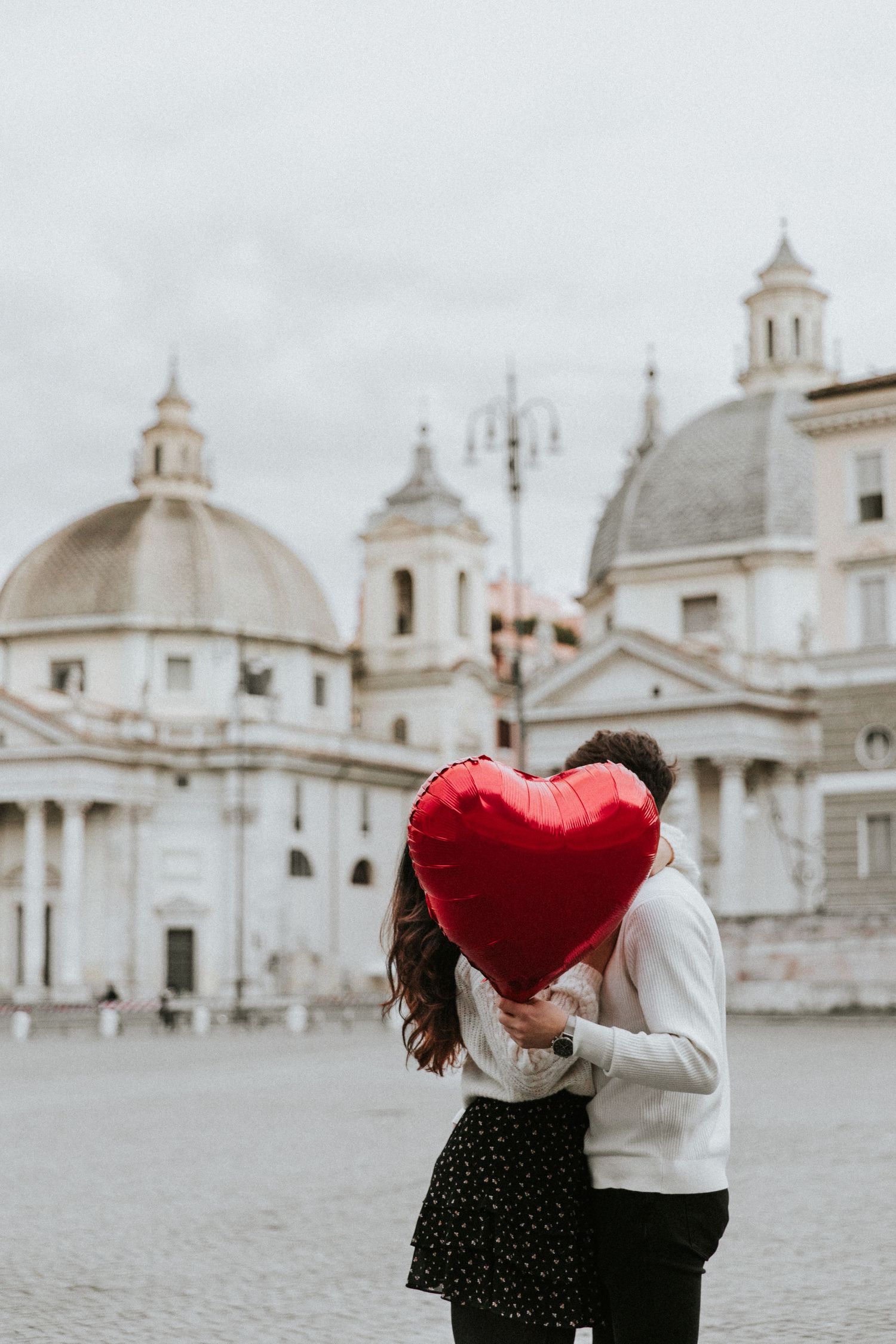 Couple kissing behind red heart balloon in Piazza del Popolo Rome on Valentine's Day.