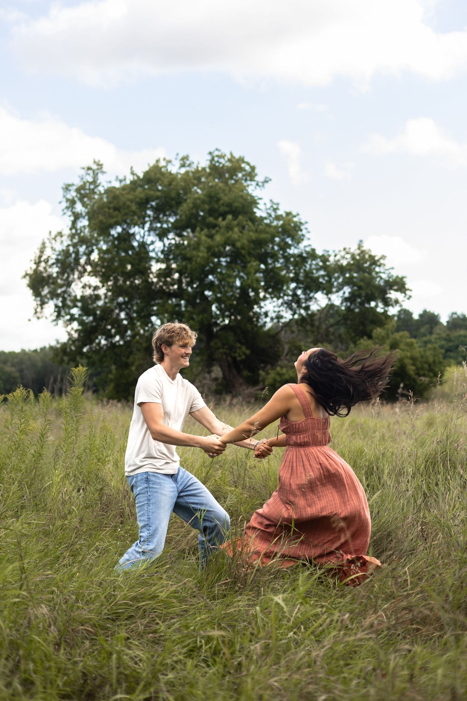 Two people dancing and spinning together in a grassy summer field with a large tree in the background.