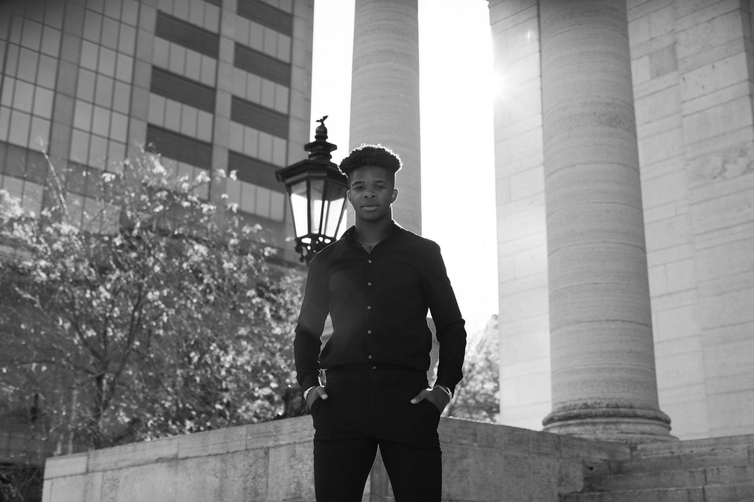 A stylish figure poses between classical architectural columns in black and white photography.