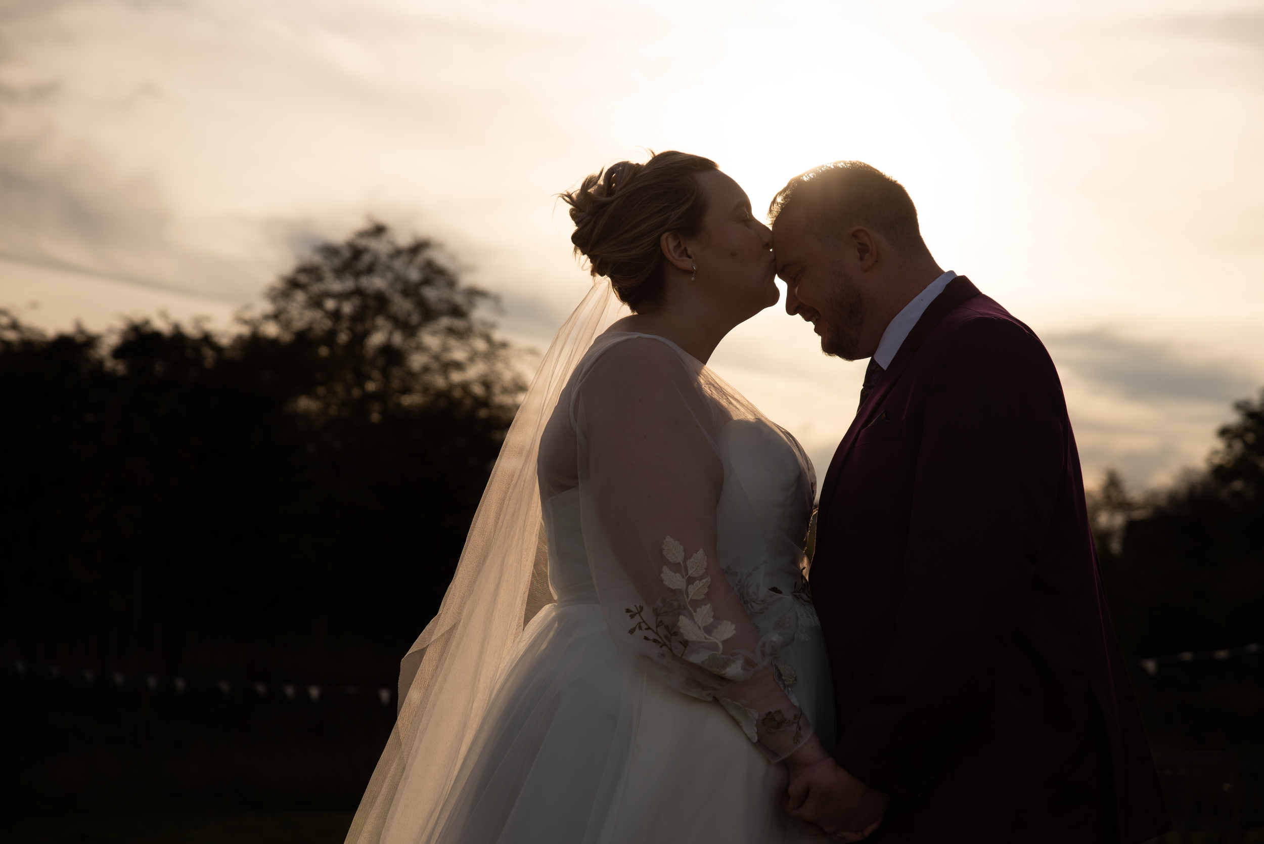Silhouetted wedding couple embracing during sunset with dramatic sky backdrop.