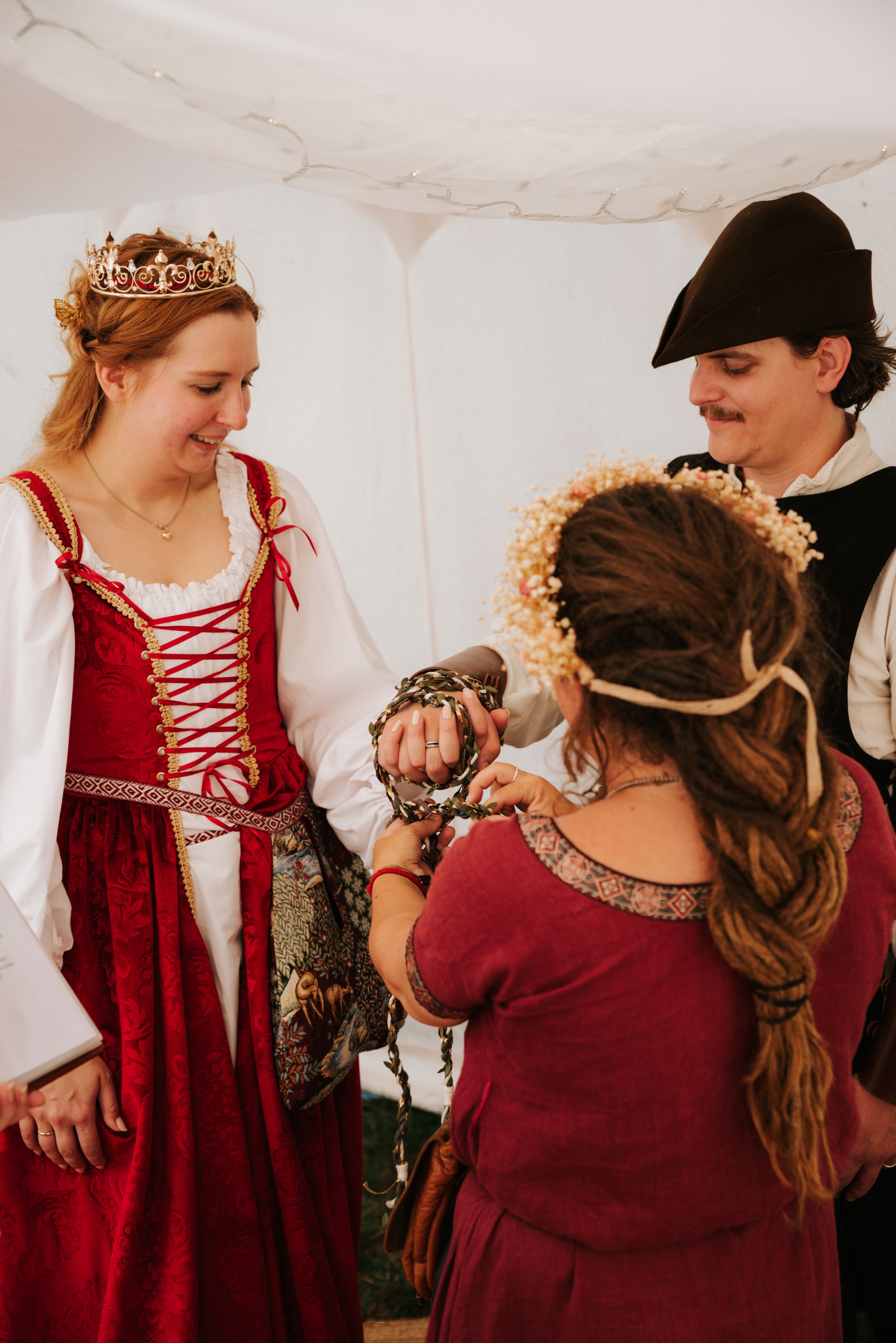 A female and male couple in medieval dress are handfasted. The celebrant ties their hands.