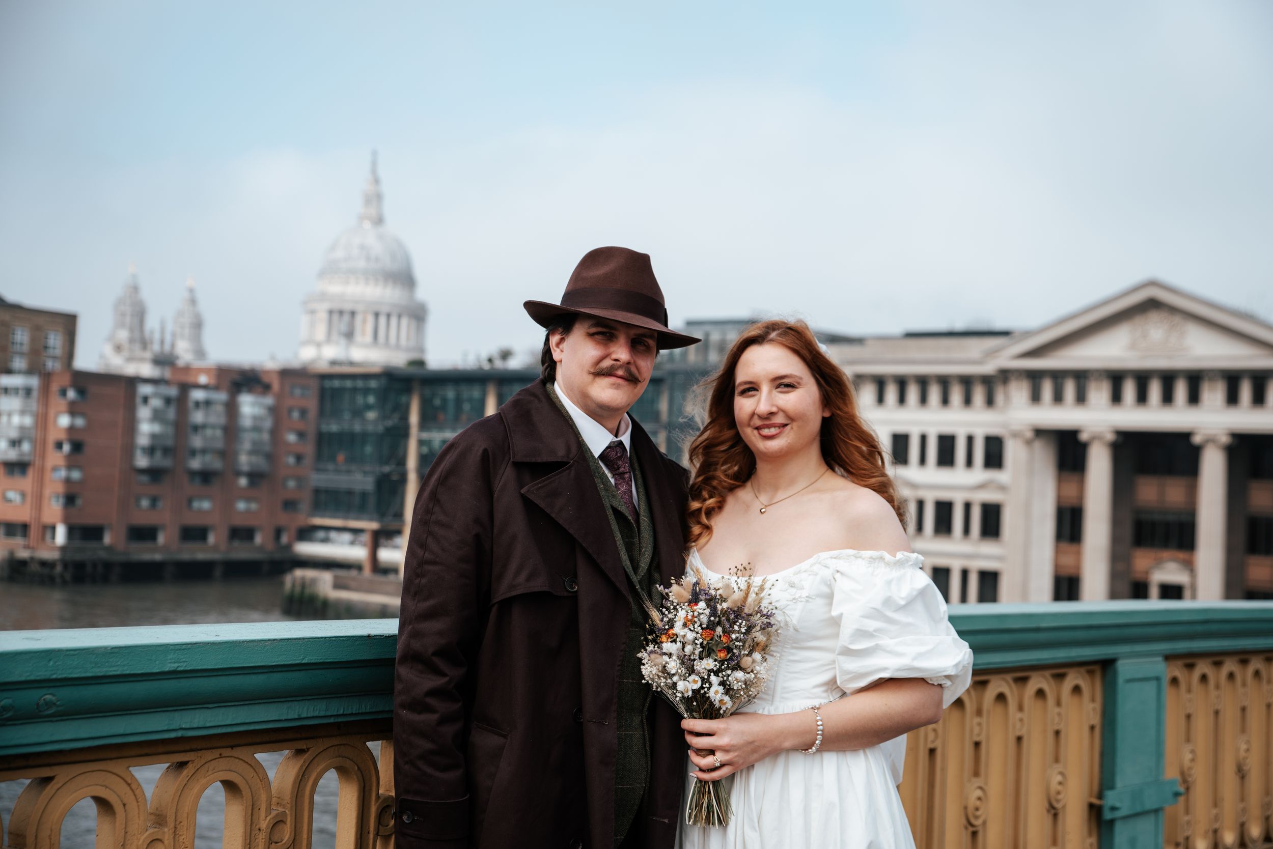 Couple in vintage attire poses on London bridge with St. Paul's Cathedral backdrop on their wedding day.