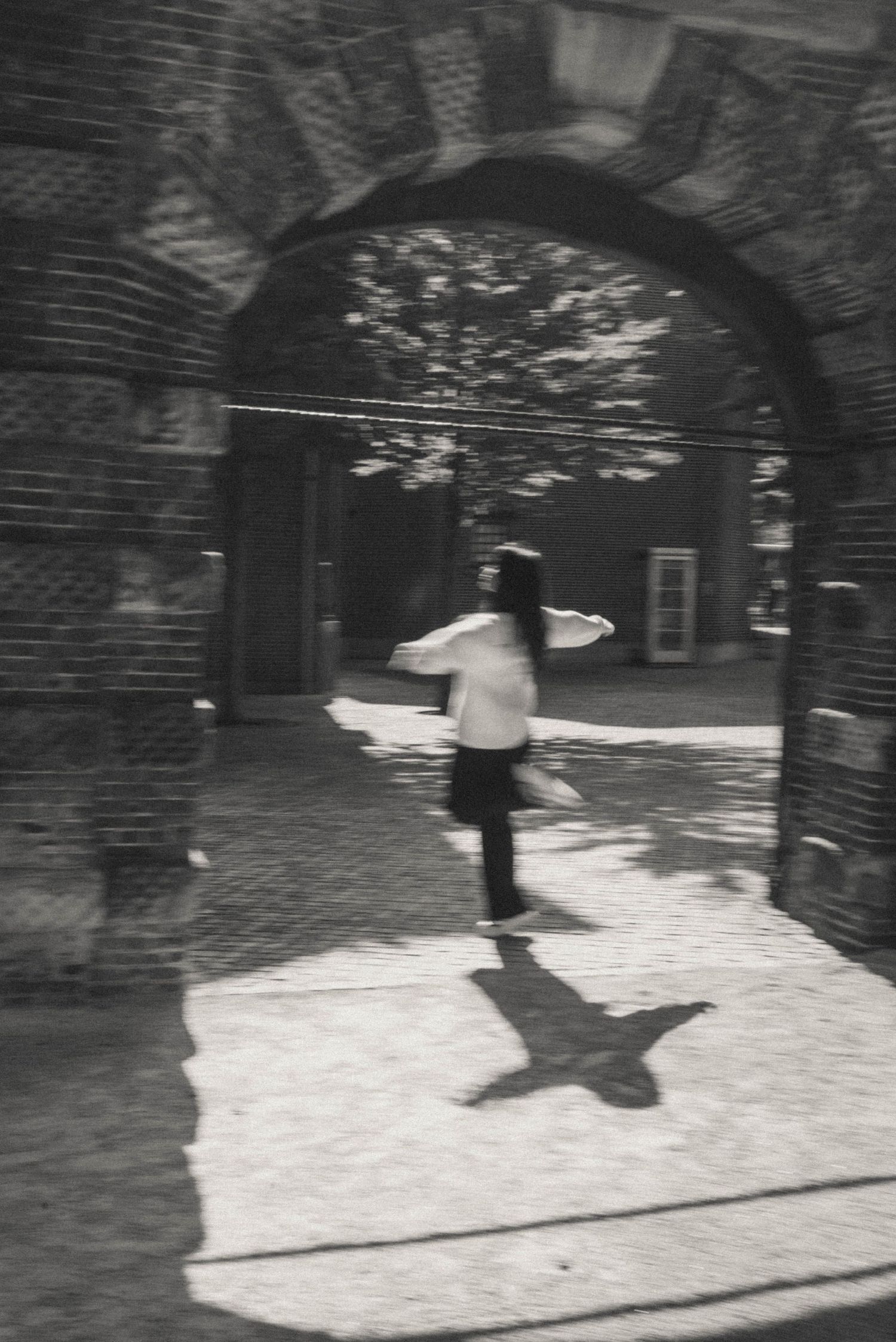 Black and white cinematic photo of a woman dancing under an ancient arch in the Rijksmuseum gardens.