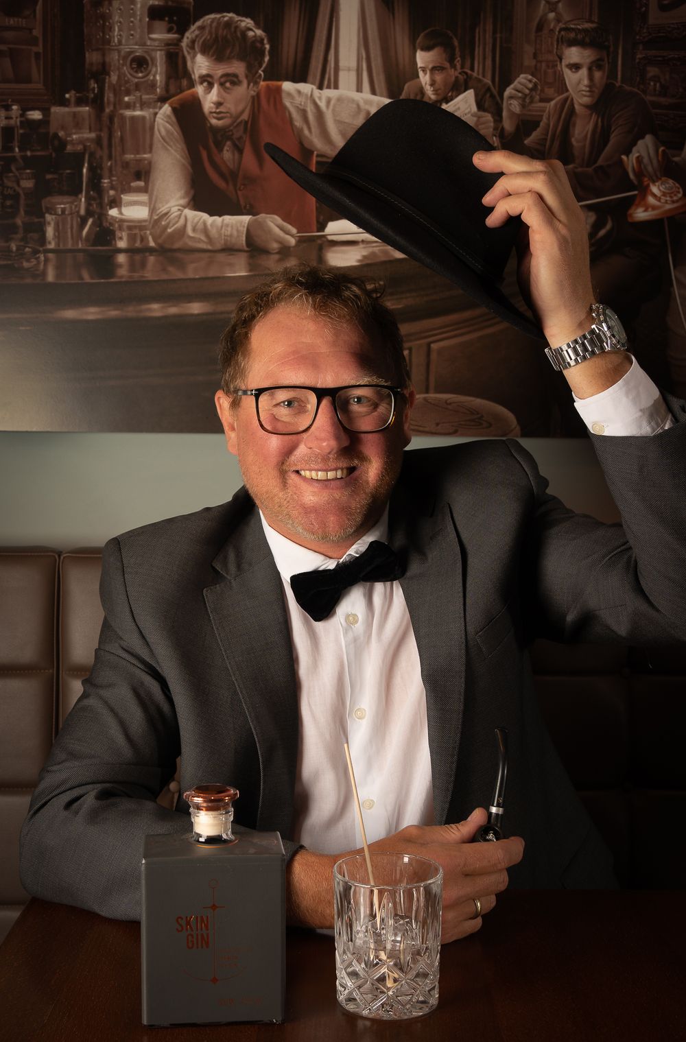 Menfotografie - a Gentleman in formal attire raising his hat at a bar with a retro scene displayed in the background.