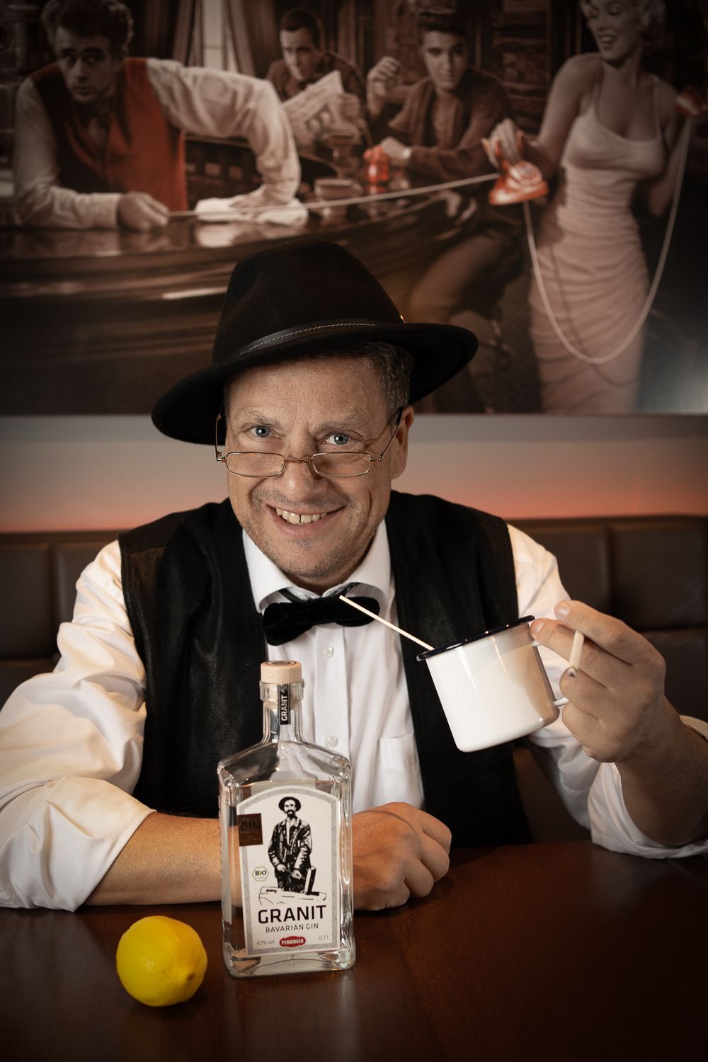 Menfotografie - a man in bow tie and hat enjoying a drink at bar with vintage scene and bottle displayed.