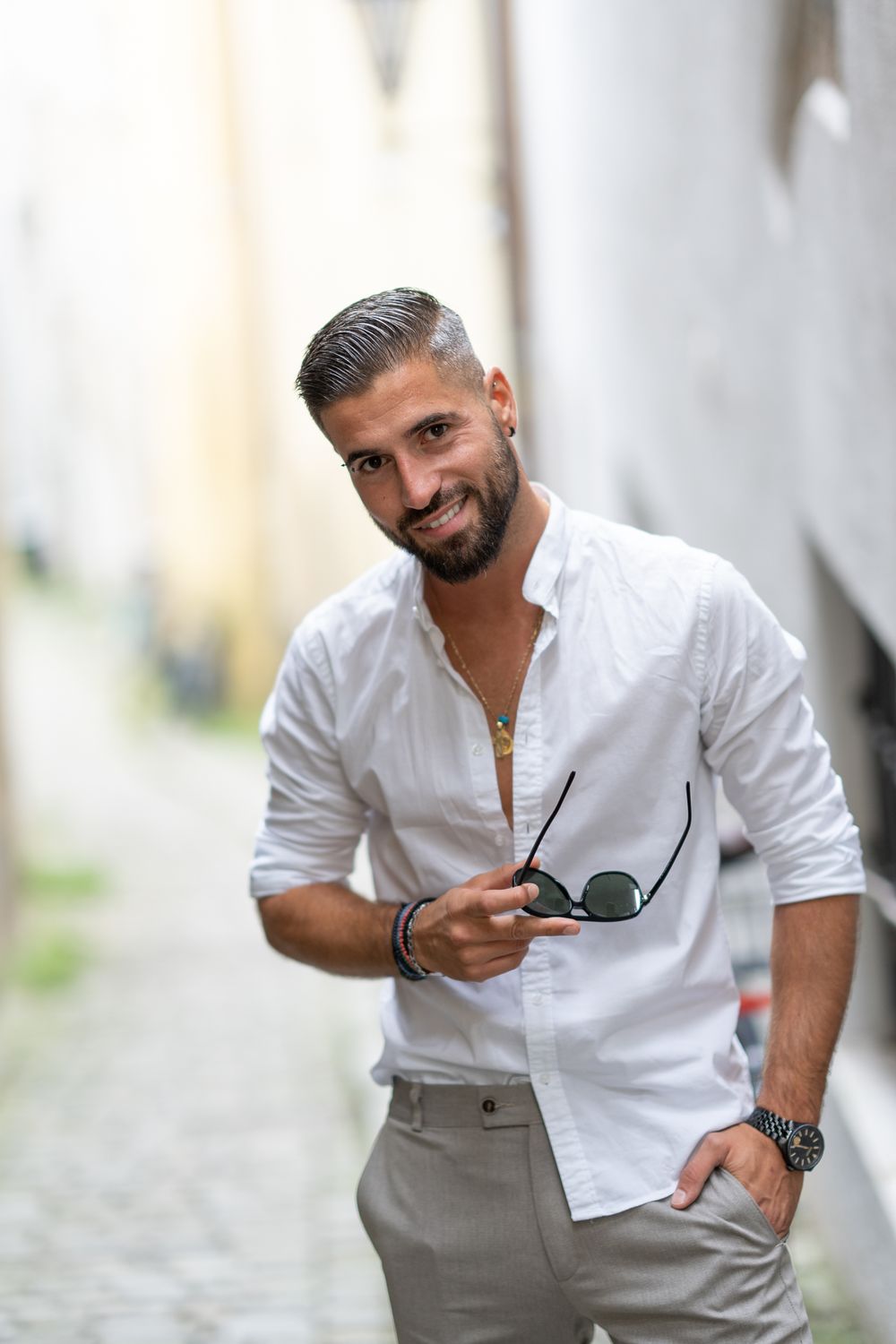 Menfotografie, Professional fashion portrait of man in white shirt holding sunglasses in urban setting.