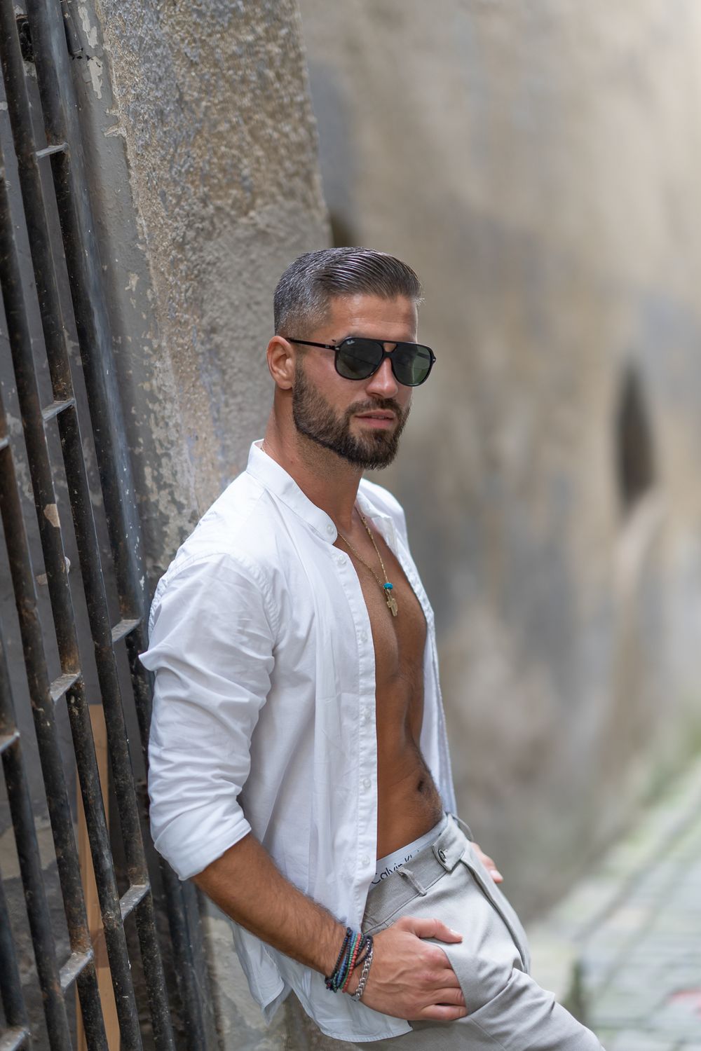 Menfotografie. Fashion photo of a stylish unbuttoned white shirt and sunglasses against an urban wall.