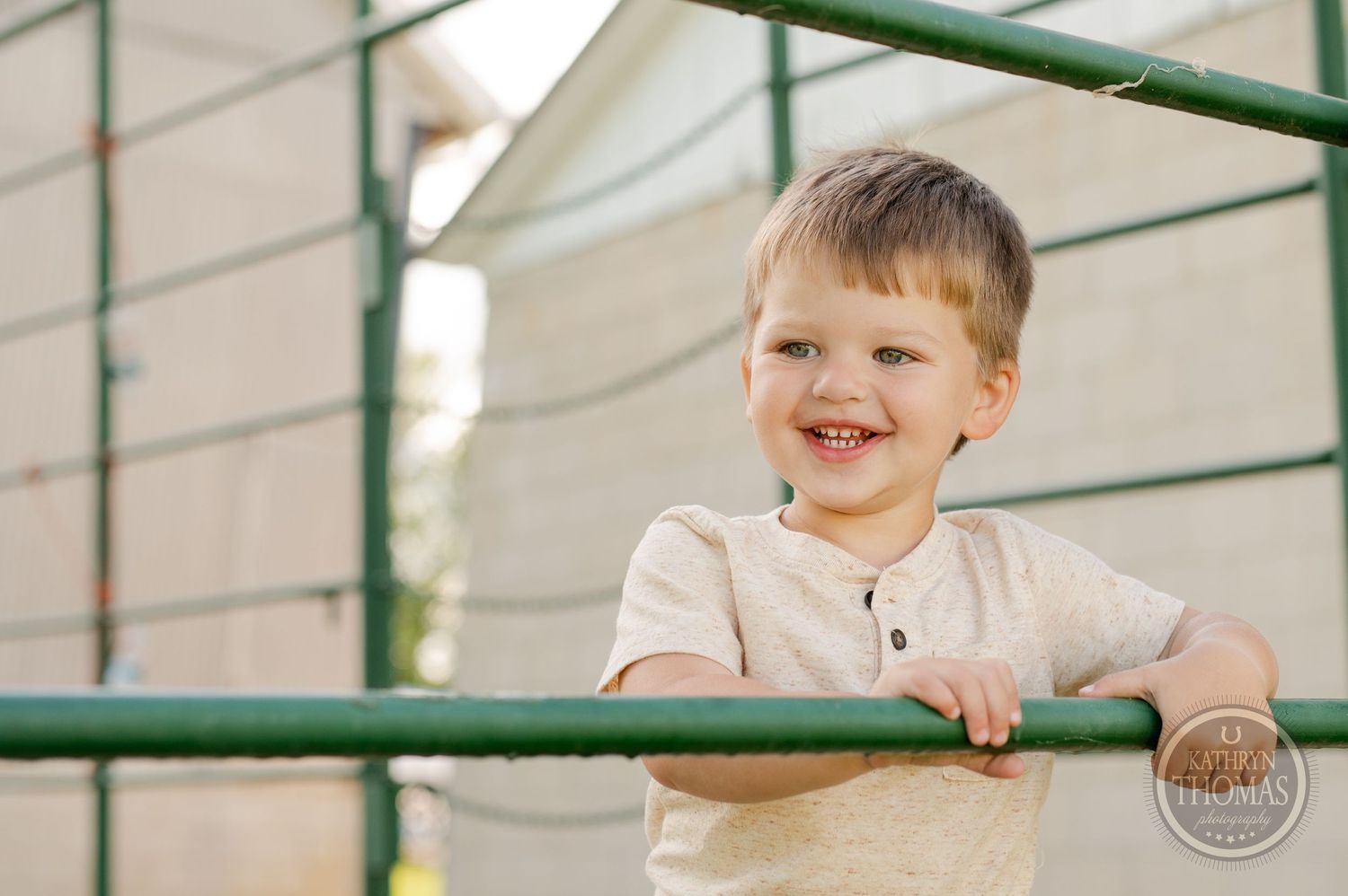 Smiling child plays on outdoor metal railings in casual attire.