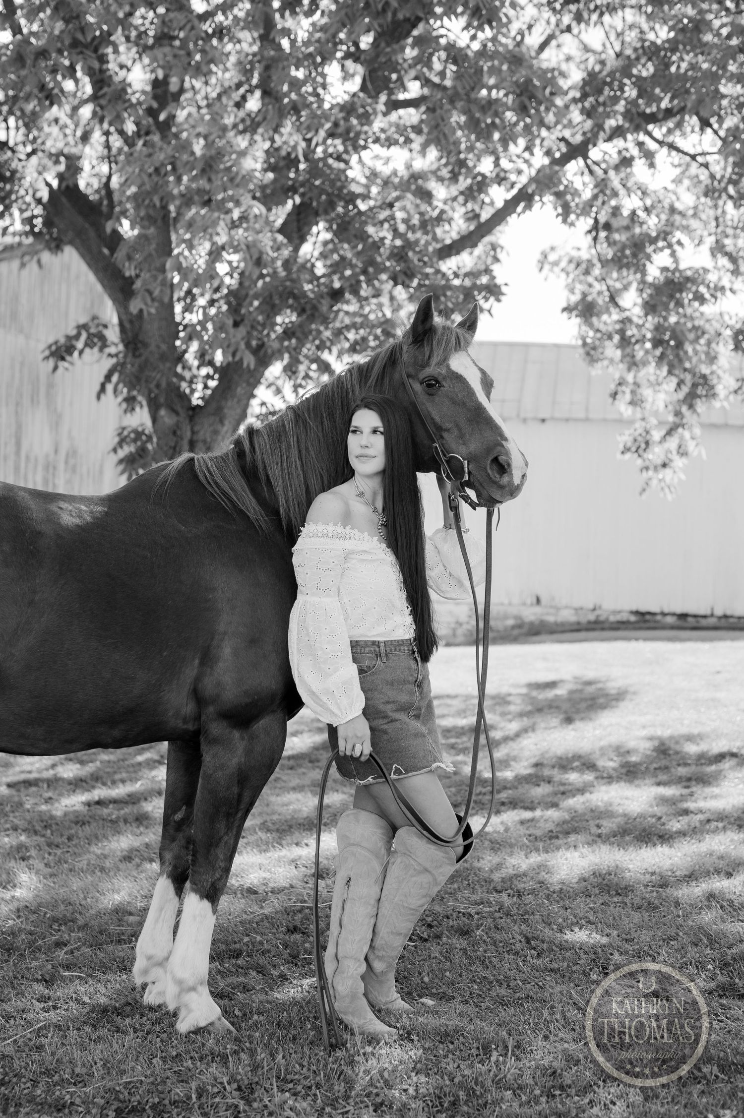 Black and white photo of a majestic horse with white socks standing near a barn.