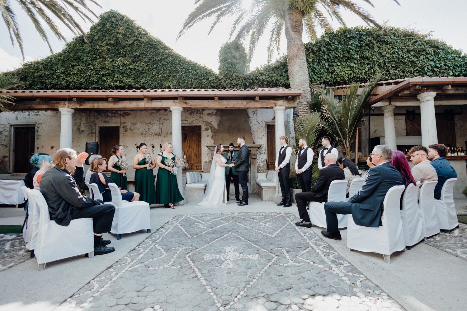 An outdoor wedding ceremony takes place at elegant Spanish-style venue, captured by Apertured Media Auckland Wedding Photographer.