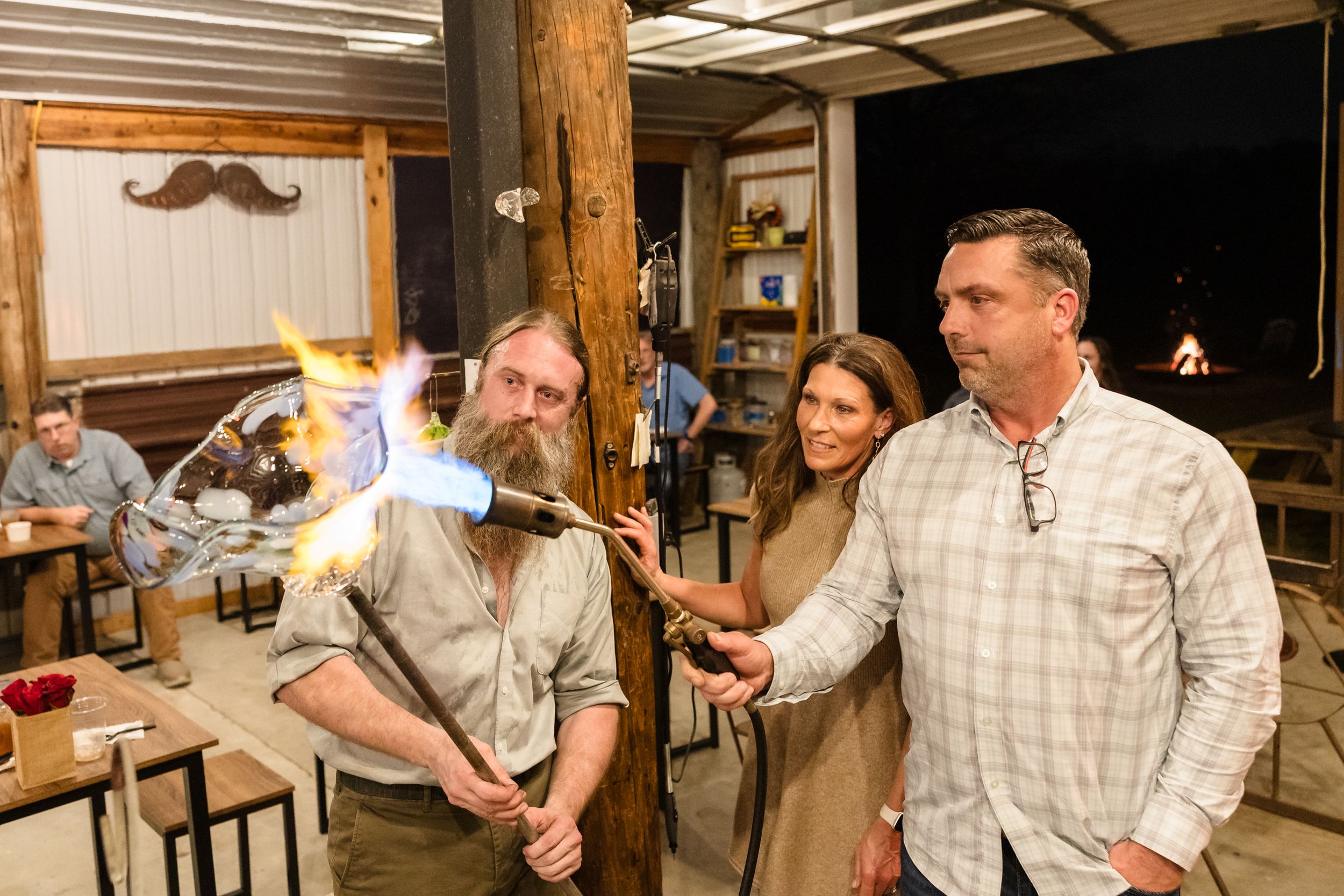 People gather in a rustic workshop setting with wooden beams and decorative mustache wall art.