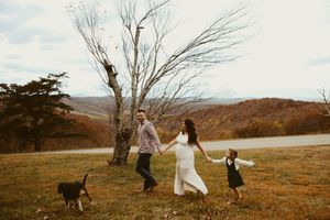 Happy family with young daughter and dog walking hand-in-hand in scenic autumn mountain landscape.
