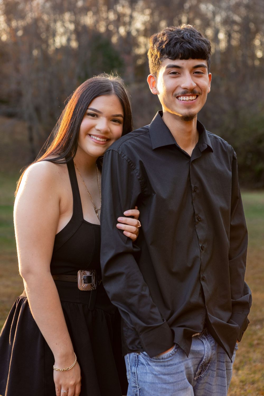 Young couple in matching black outfits smiling together outdoors during golden hour in a field.