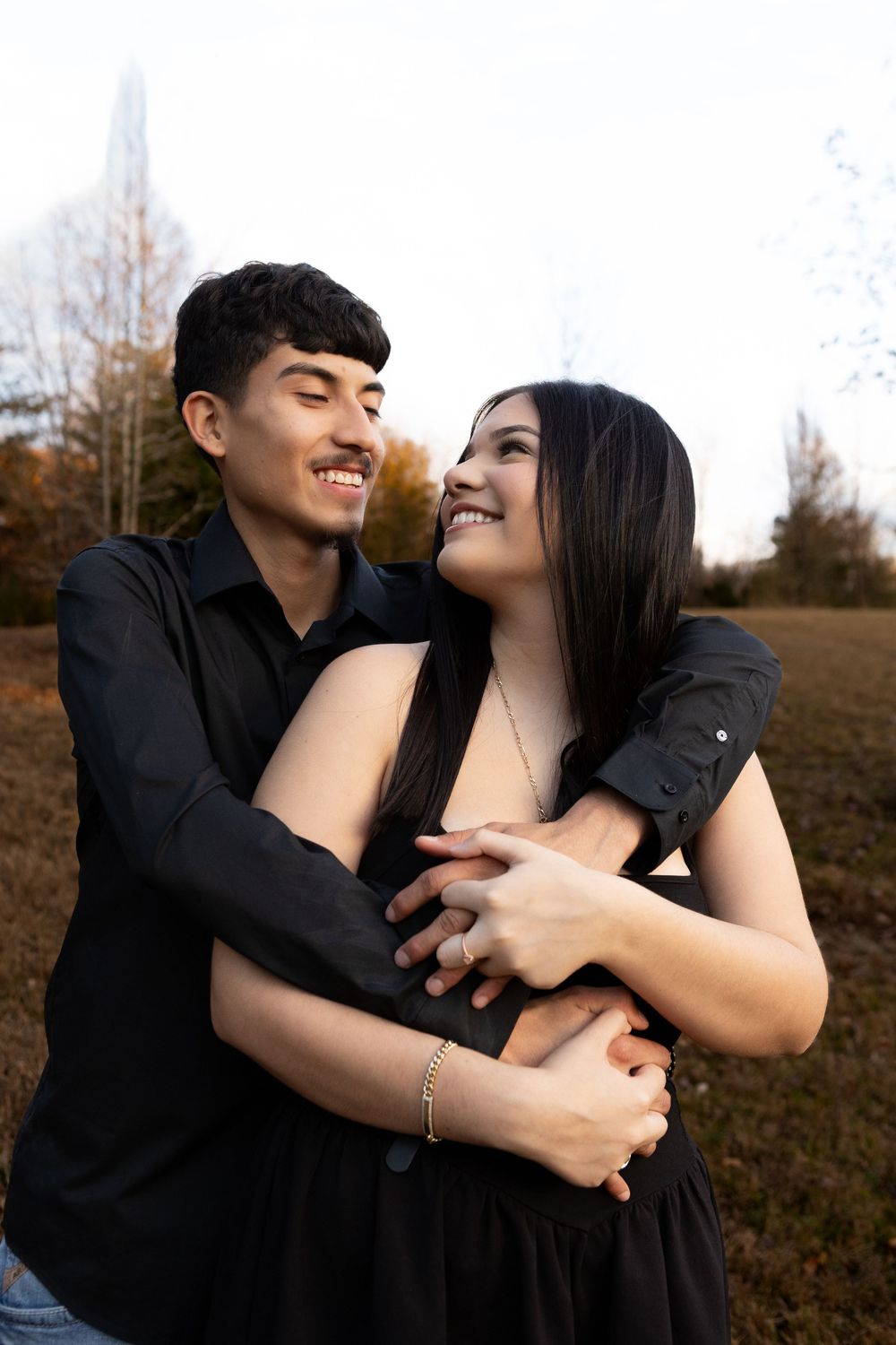 Young couple embracing and smiling together in a field during an outdoor couples photo session.