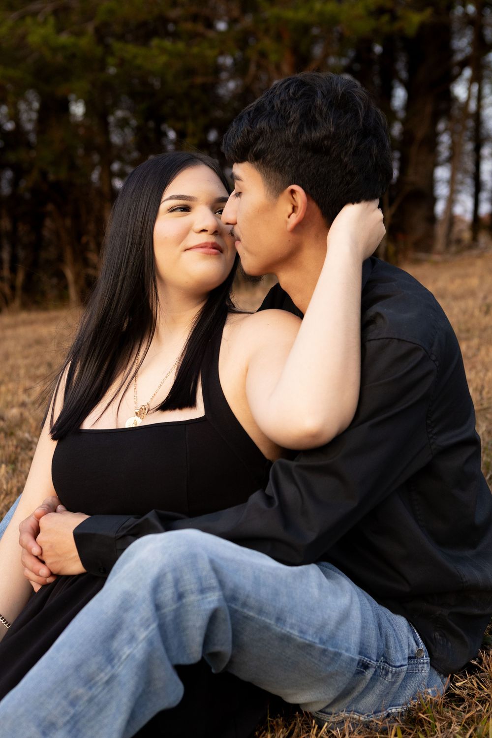 Romantic young couple sitting closely together in a field, sharing a tender moment outdoors.