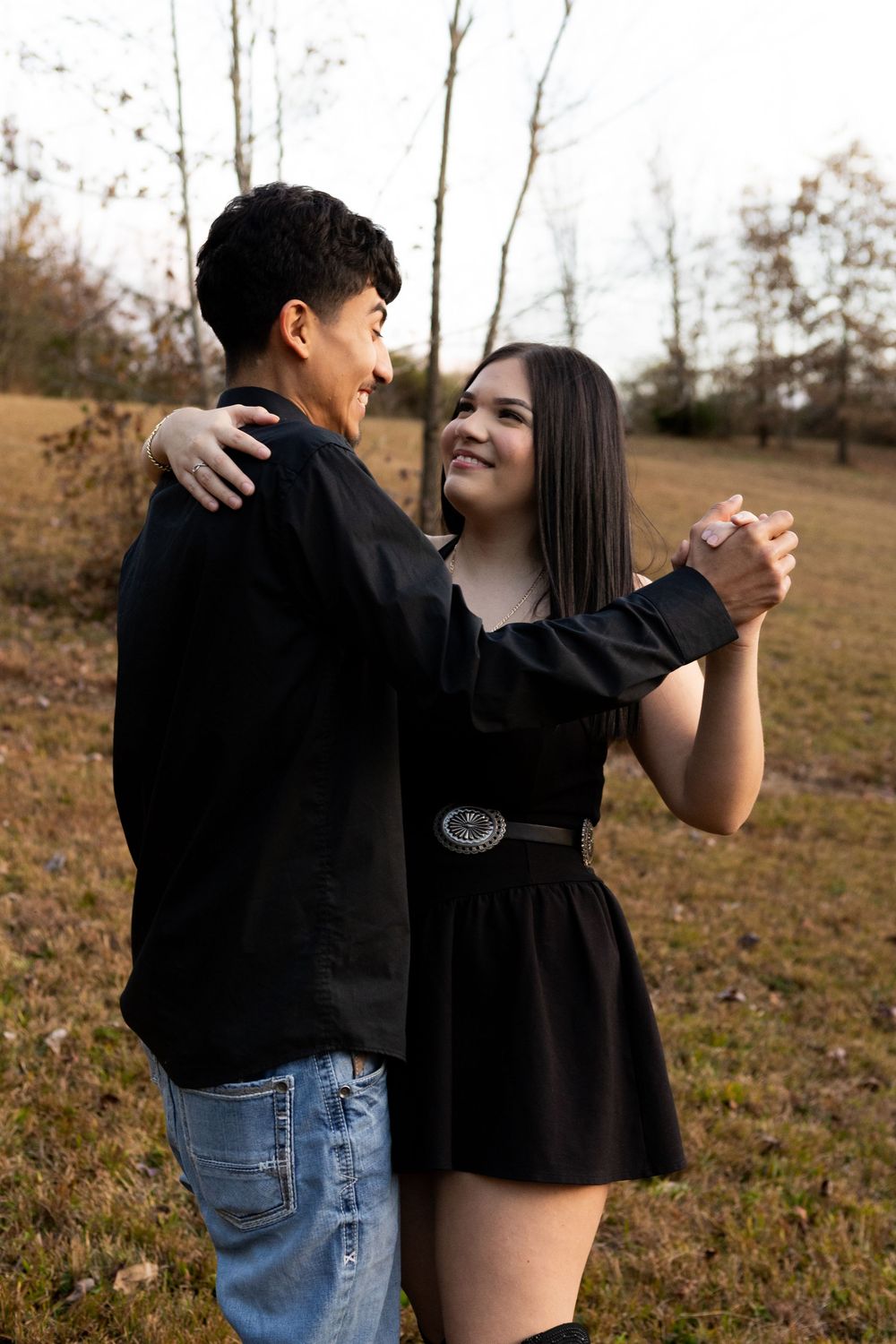 Young couple dancing together outdoors in a field, smiling and holding hands at golden hour.
