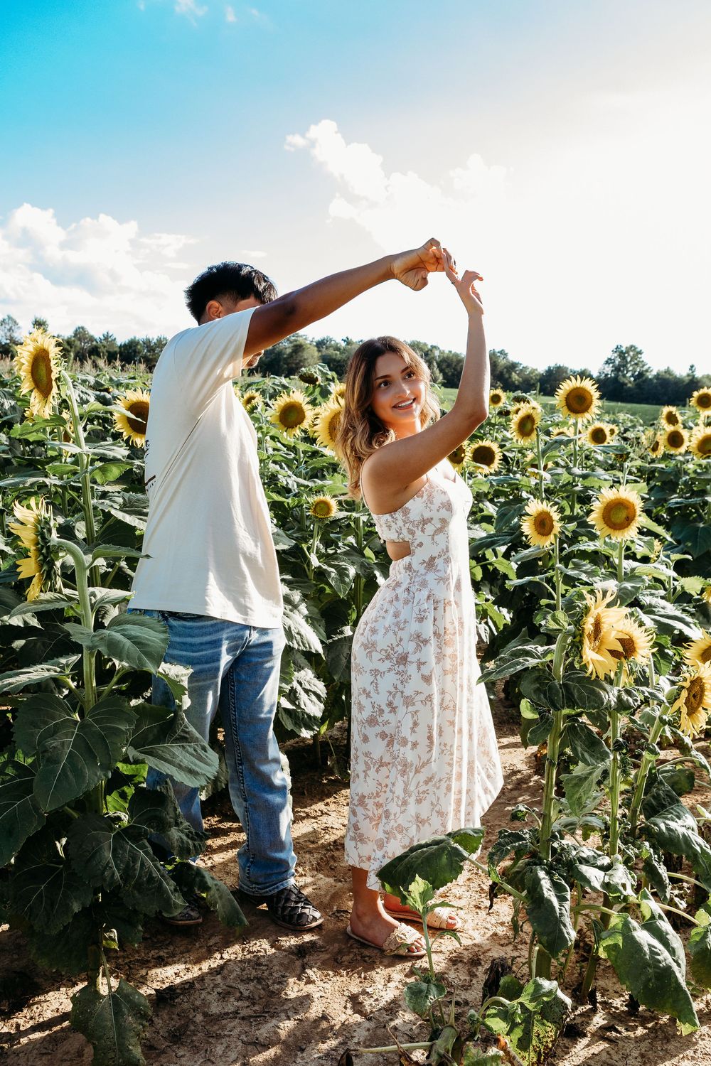 Young couple dancing together in a vibrant sunflower field under a bright blue summer sky.