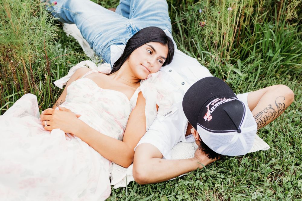 Couple lying in green grass together, woman in white dress smiling at camera.