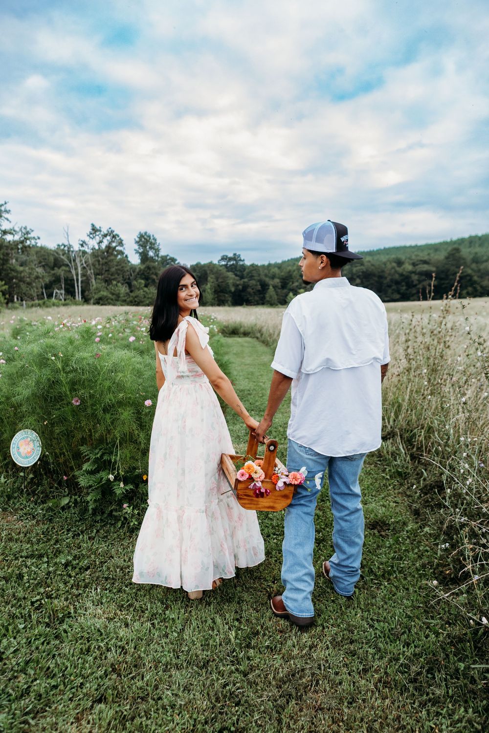 Couple walking hand in hand carrying a flower basket through a lush green meadow.