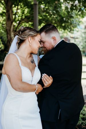 Bride and groom touching foreheads tenderly in an outdoor garden setting on their wedding day.