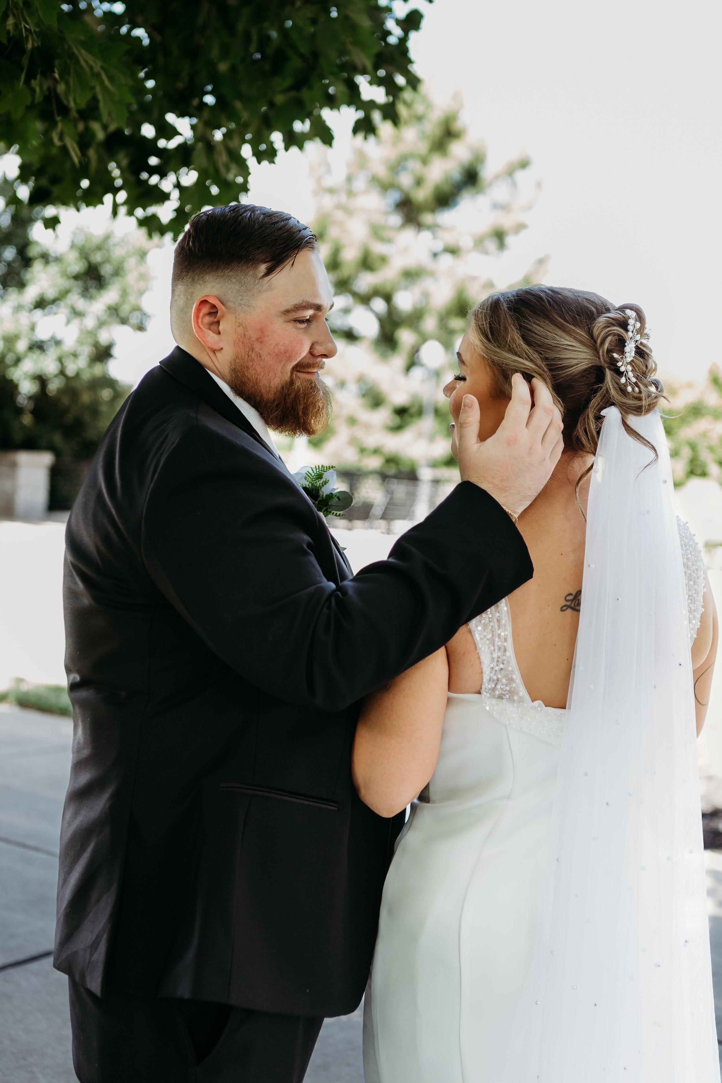 Groom tenderly cradling bride's face while she smiles during outdoor wedding portrait session.