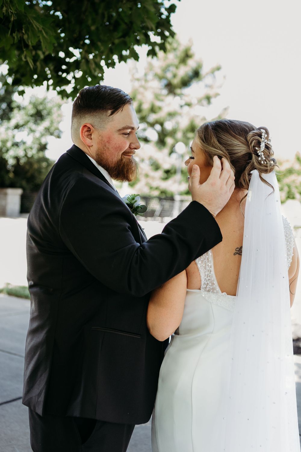 Groom tenderly cradling bride's face while she smiles during outdoor wedding portrait session.