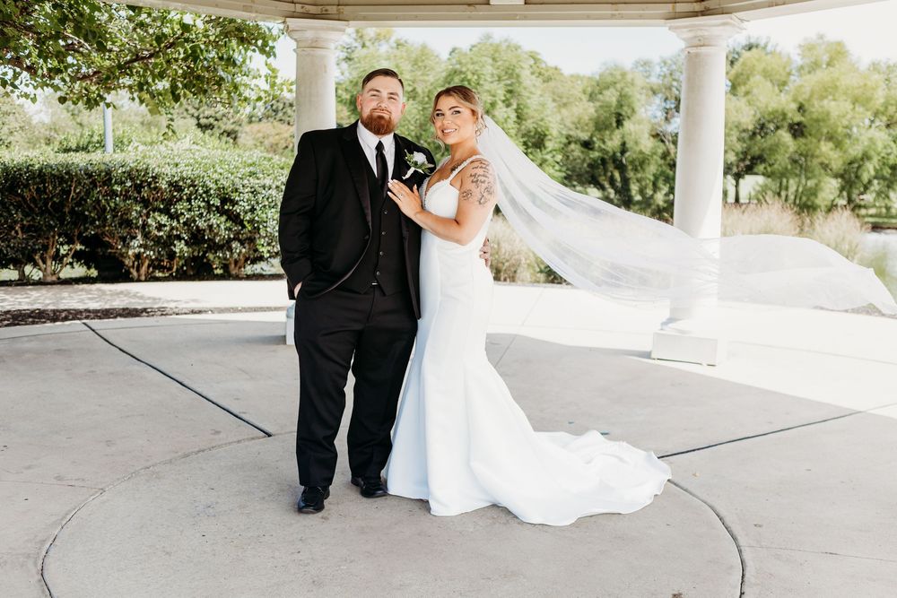 Bride and groom posing elegantly under white pavilion, bride's veil flowing in the breeze.