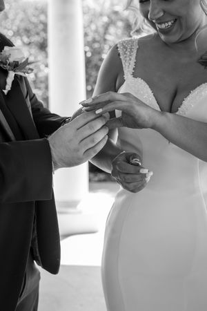 Black and white photo of bride placing wedding ring on grooms finger during ceremony.