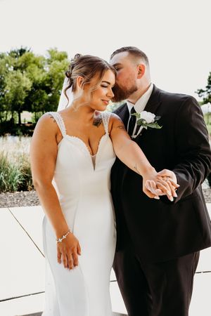 Bride and groom share a tender kiss outdoors, showcasing their wedding rings and elegant attire.