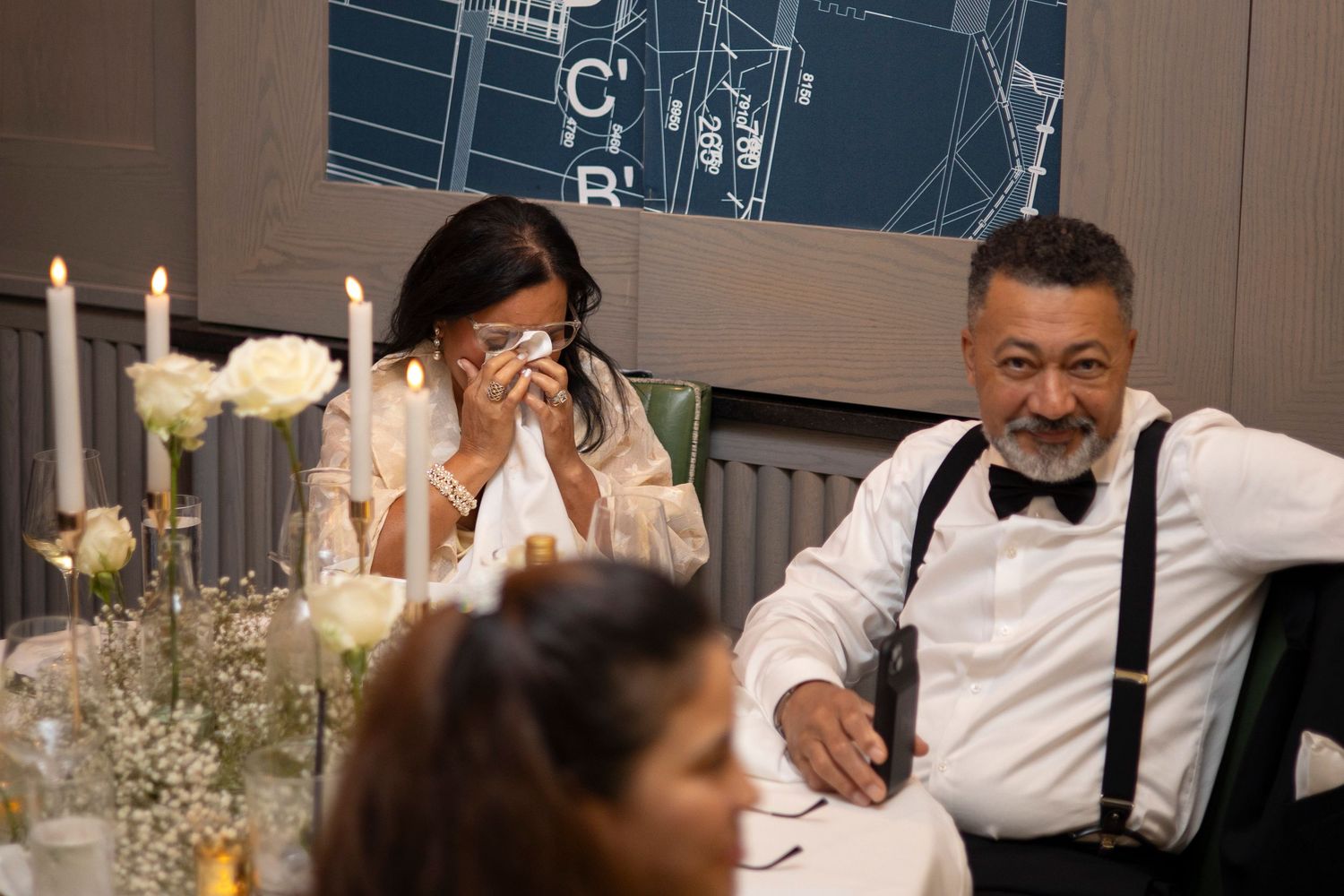 A group of wedding guests share emotional reactions during a reception celebration.