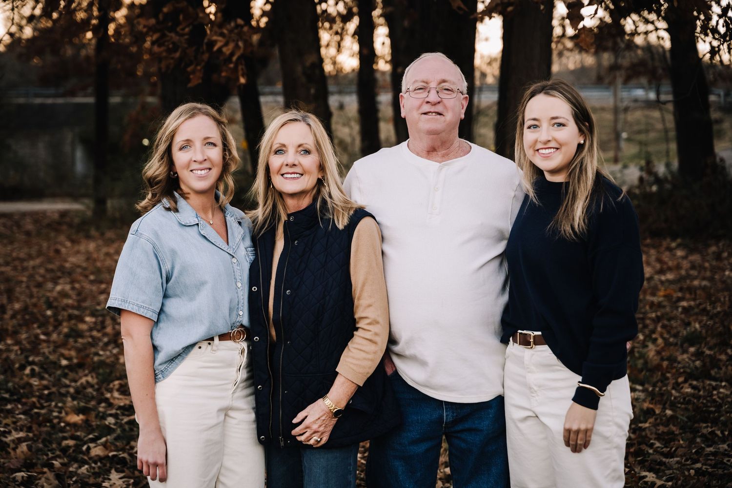 parents and adult daughters stands together outdoors on fallen autumn leaves during a fall photoshoot. Family photographer in Middle Tenness