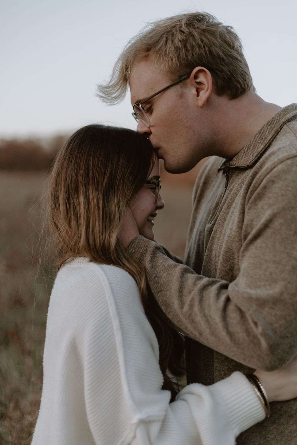 Couple sharing a tender forehead kiss in an autumn field at dusk.